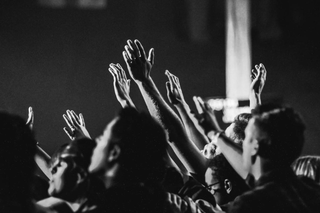 Dynamic black and white photo of a concert audience with hands raised, capturing the energy of live music.